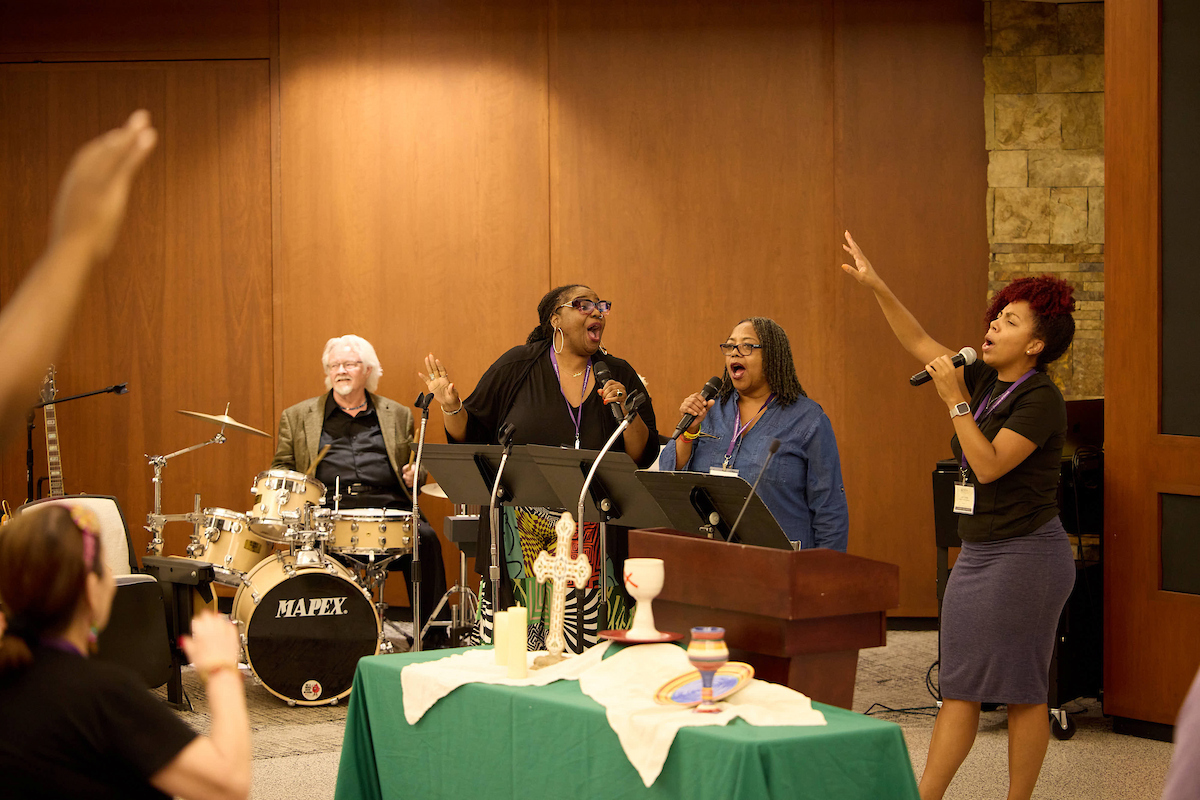 Three women joyfully singing in a place of worship.