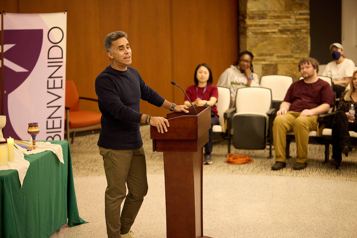 A man speaking to a small group of people with a bienvenido banner in the background